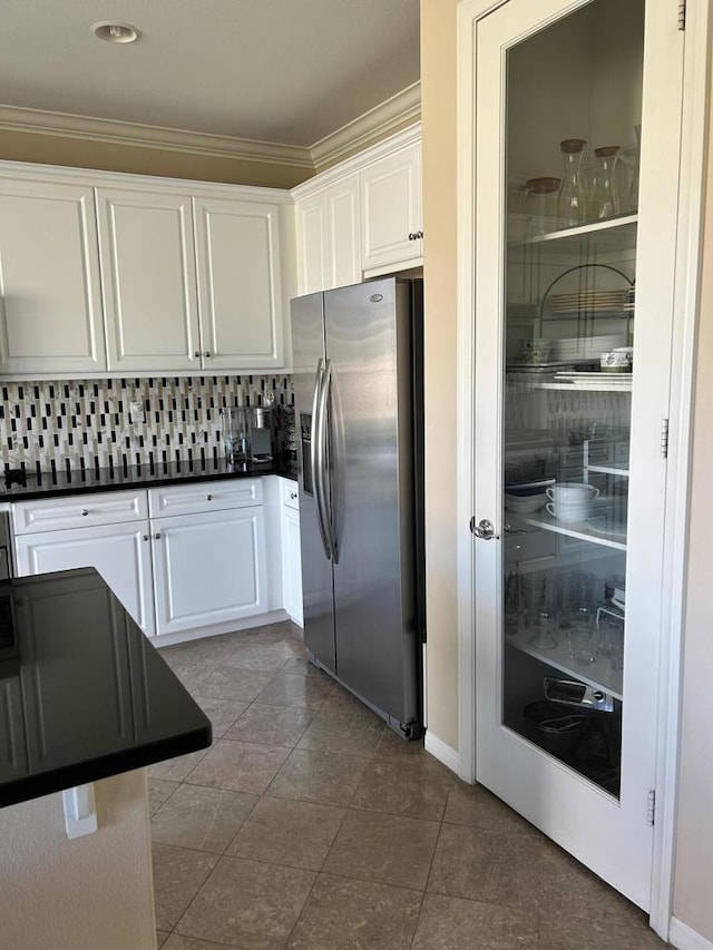 kitchen featuring stainless steel refrigerator with ice dispenser, white cabinetry, crown molding, dark tile patterned floors, and backsplash