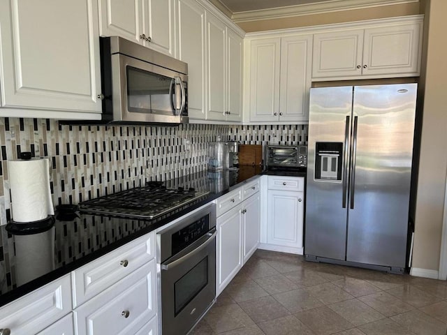 kitchen featuring appliances with stainless steel finishes, dark stone countertops, white cabinets, backsplash, and light tile patterned floors