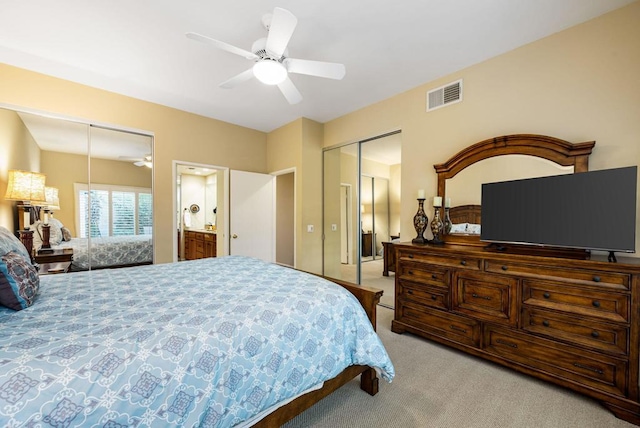 bedroom with multiple closets, light colored carpet, ensuite bathroom, and ceiling fan