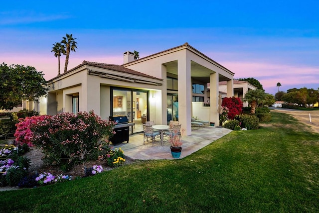 back house at dusk with a yard and a patio