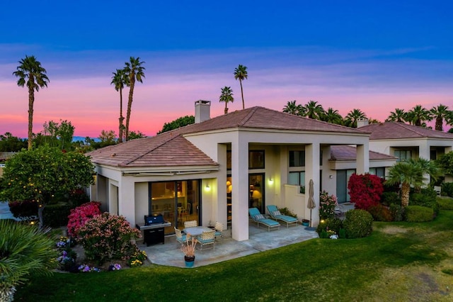 back house at dusk with a yard and a patio