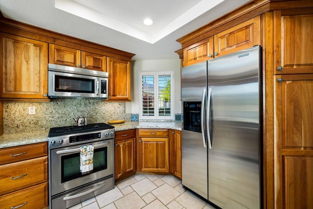 kitchen with light stone counters, stainless steel appliances, a tray ceiling, and decorative backsplash