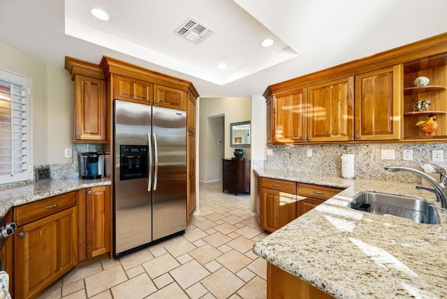 kitchen featuring sink, stainless steel refrigerator with ice dispenser, light stone counters, tasteful backsplash, and a raised ceiling