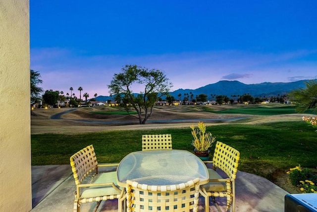 patio terrace at dusk featuring a mountain view and a lawn