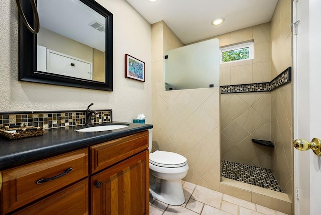 bathroom featuring tiled shower, toilet, vanity, tile patterned flooring, and decorative backsplash