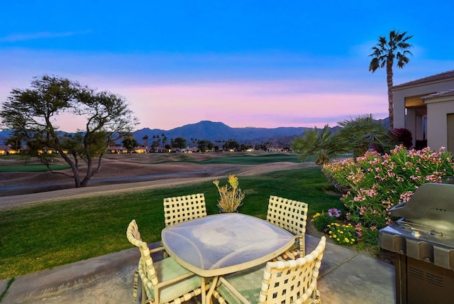 patio terrace at dusk featuring a mountain view, a lawn, and a grill