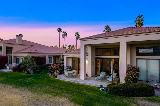 back house at dusk featuring a patio area and a lawn