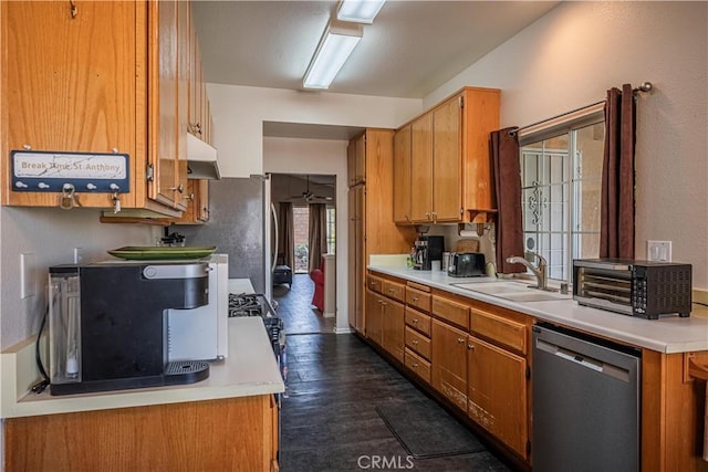 kitchen featuring brown cabinetry, stainless steel appliances, light countertops, under cabinet range hood, and a sink