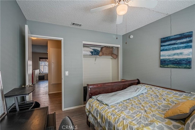 bedroom with a textured ceiling, visible vents, a ceiling fan, a closet, and dark wood finished floors