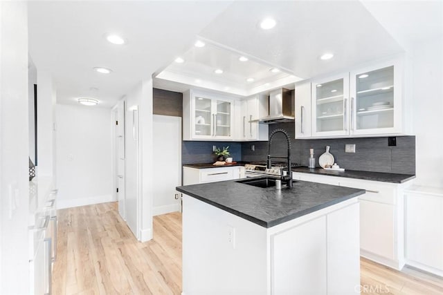 kitchen featuring wall chimney exhaust hood, sink, a kitchen island with sink, light hardwood / wood-style floors, and white cabinets