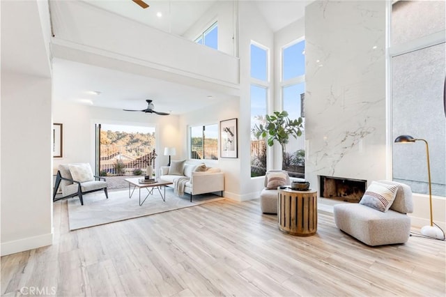 living room featuring ceiling fan, a premium fireplace, a high ceiling, and light wood-type flooring