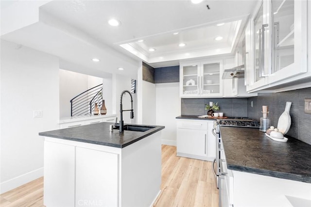 kitchen with sink, white cabinetry, a tray ceiling, a center island with sink, and gas range