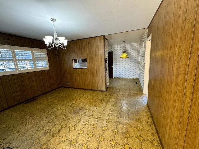 unfurnished dining area featuring wooden walls, a chandelier, and brick wall