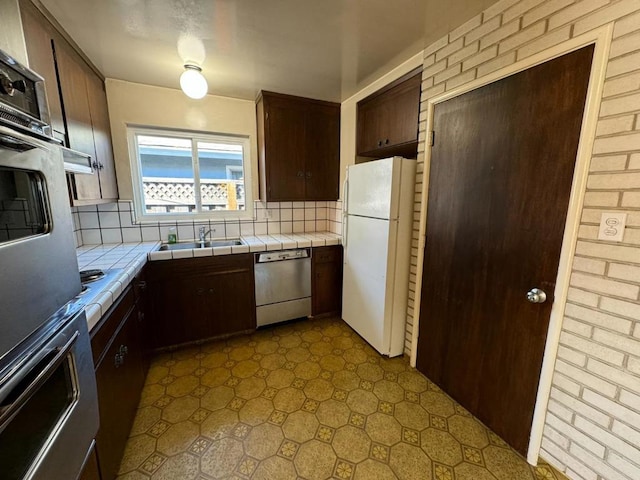 kitchen with tile countertops, sink, backsplash, dark brown cabinetry, and white appliances