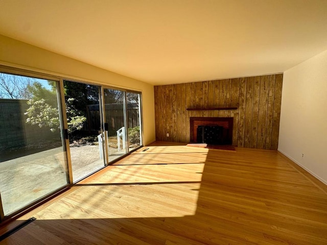 unfurnished living room featuring wood-type flooring, a brick fireplace, and wood walls