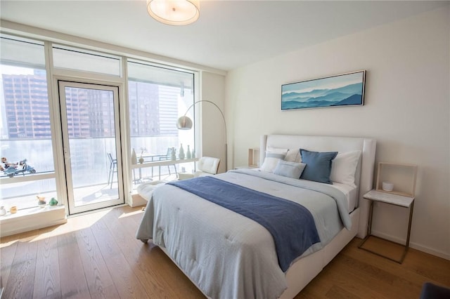 bedroom featuring access to exterior, a wall of windows, and light hardwood / wood-style flooring