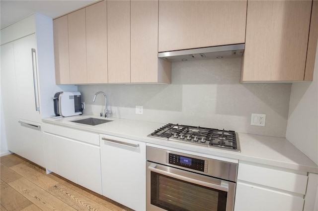 kitchen with appliances with stainless steel finishes, sink, and light hardwood / wood-style flooring