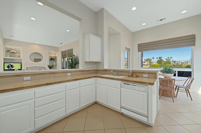 kitchen featuring sink, light tile patterned floors, white dishwasher, kitchen peninsula, and white cabinets