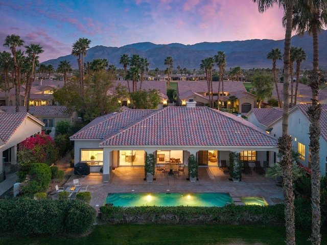 back house at dusk with a mountain view and a patio area