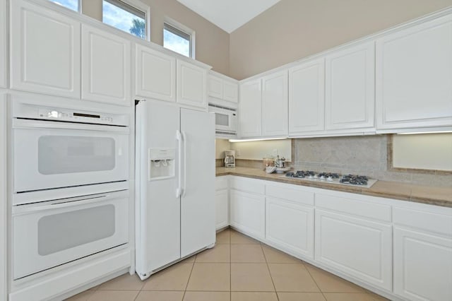 kitchen featuring light tile patterned floors, white appliances, white cabinets, and backsplash