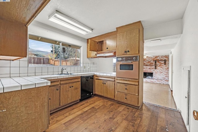 kitchen with sink, light hardwood / wood-style flooring, black dishwasher, tile countertops, and oven