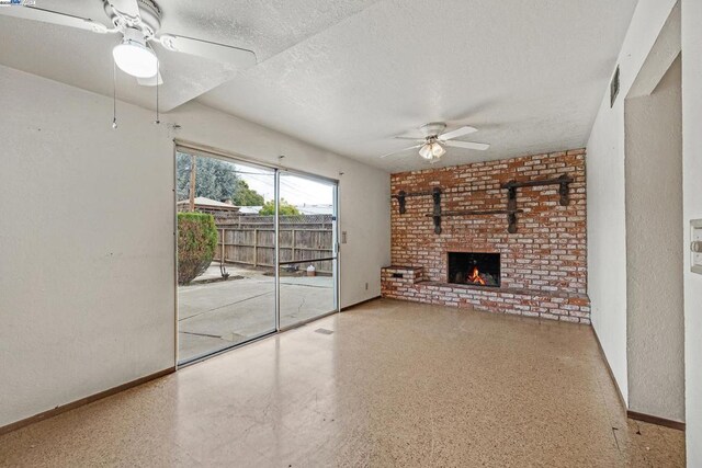 unfurnished living room featuring ceiling fan, a brick fireplace, and a textured ceiling