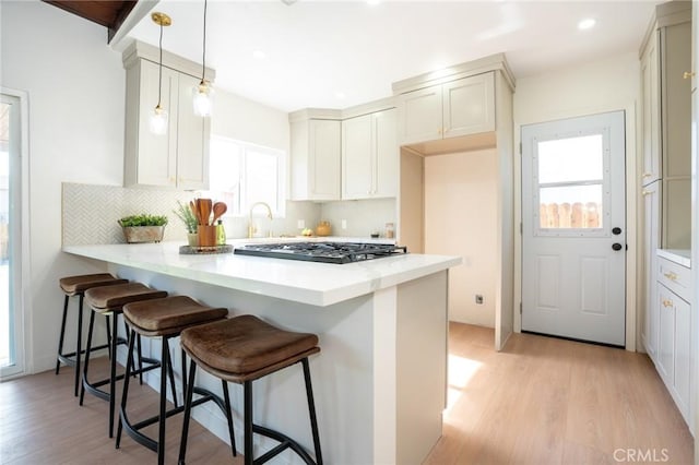 kitchen featuring decorative light fixtures, a kitchen bar, decorative backsplash, kitchen peninsula, and light wood-type flooring