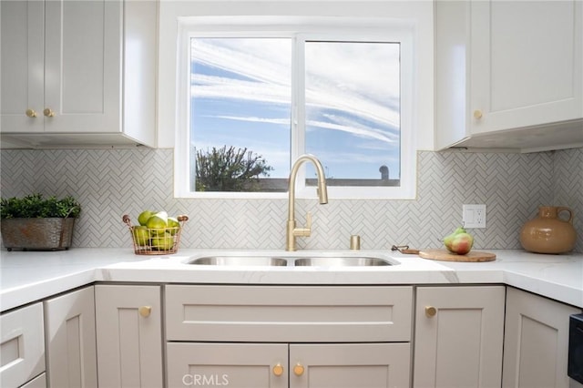 kitchen with white cabinets, sink, backsplash, and light stone counters