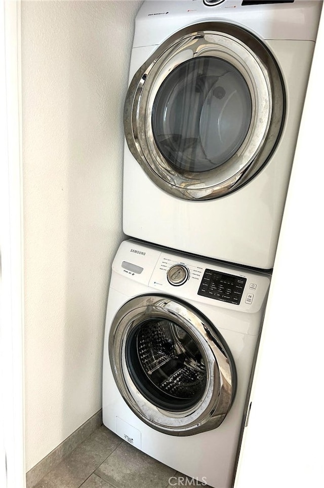 laundry area with dark tile patterned floors and stacked washer / dryer