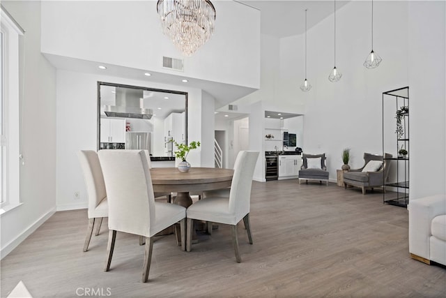 dining room with a towering ceiling, beverage cooler, light hardwood / wood-style flooring, and a notable chandelier