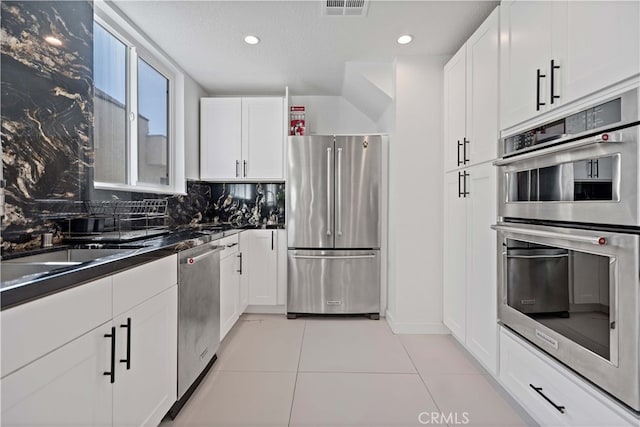 kitchen featuring appliances with stainless steel finishes, white cabinetry, decorative backsplash, light tile patterned floors, and a textured ceiling