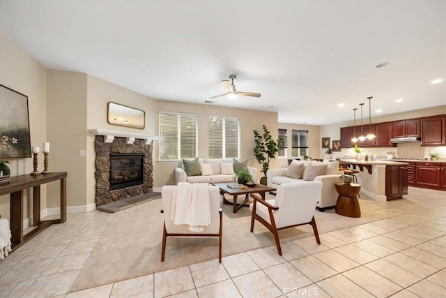 living room featuring ceiling fan, a stone fireplace, and light tile patterned floors