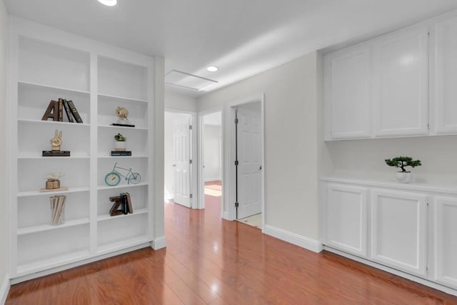 hall with built in shelves and light wood-type flooring