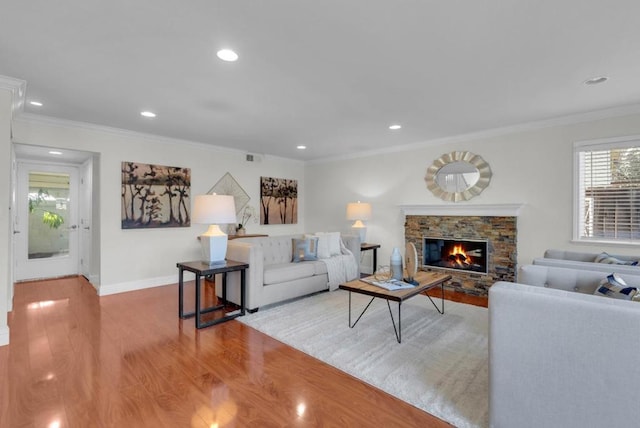 living room featuring crown molding, a stone fireplace, and light wood-type flooring