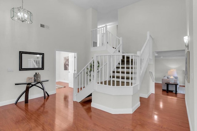 stairway featuring a towering ceiling, hardwood / wood-style floors, and a chandelier