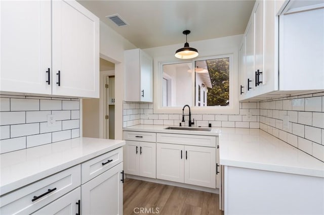 kitchen with sink, white cabinetry, light hardwood / wood-style flooring, pendant lighting, and backsplash