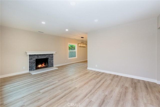 unfurnished living room with a stone fireplace, a chandelier, and light hardwood / wood-style flooring