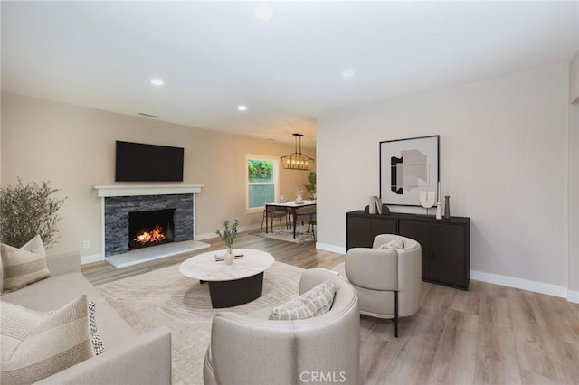 living area with light wood finished floors, baseboards, a stone fireplace, and recessed lighting