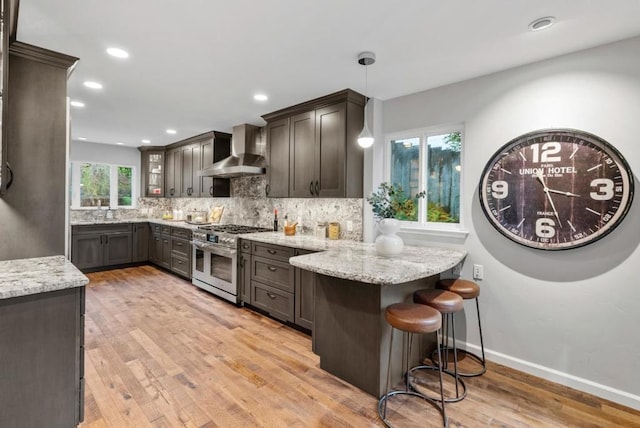 kitchen with hanging light fixtures, light stone counters, kitchen peninsula, wall chimney exhaust hood, and range with two ovens