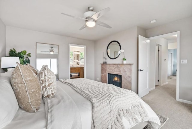 bedroom featuring light carpet, ensuite bath, a premium fireplace, and ceiling fan