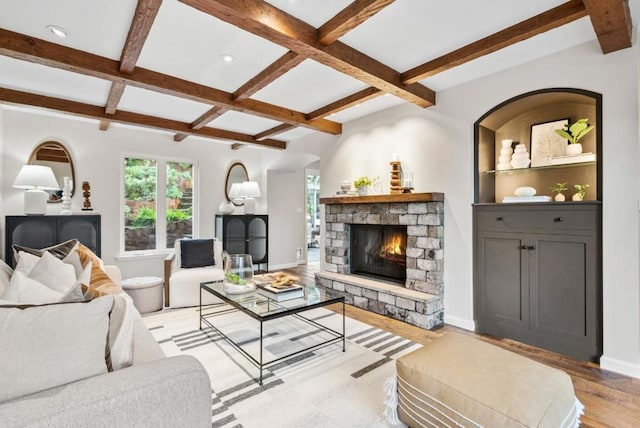 living room with beam ceiling, a stone fireplace, and light hardwood / wood-style floors