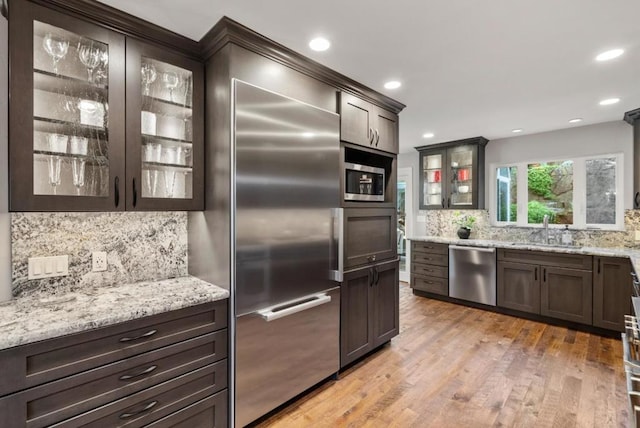 kitchen with sink, tasteful backsplash, built in appliances, light hardwood / wood-style flooring, and light stone countertops