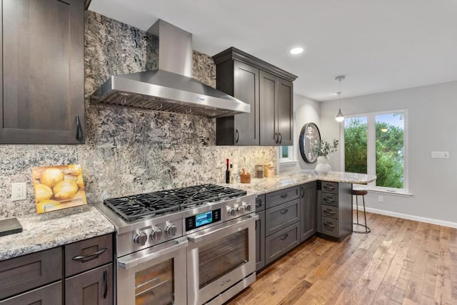 kitchen with double oven range, hanging light fixtures, tasteful backsplash, a kitchen bar, and wall chimney exhaust hood