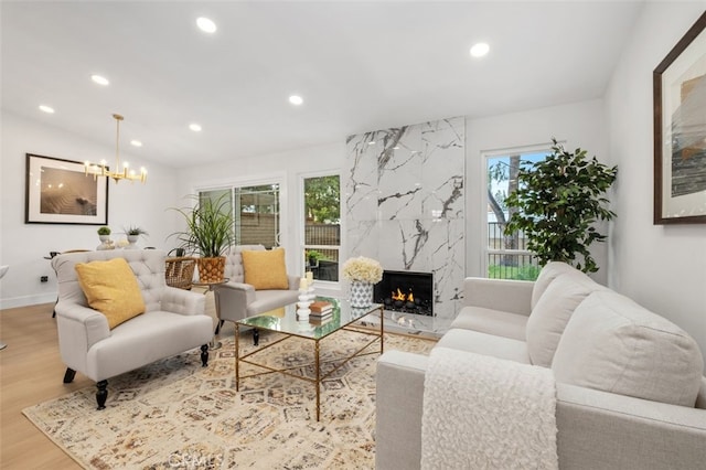 living room with lofted ceiling, a high end fireplace, a chandelier, and light hardwood / wood-style floors