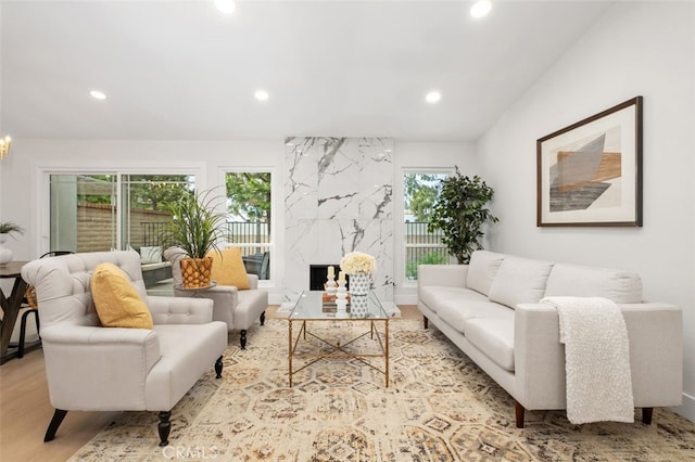 living room with a high end fireplace, light hardwood / wood-style floors, a healthy amount of sunlight, and vaulted ceiling