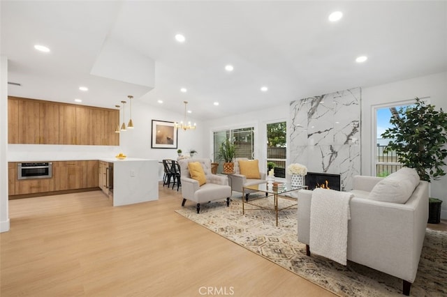 living room with an inviting chandelier, plenty of natural light, a premium fireplace, and light hardwood / wood-style floors