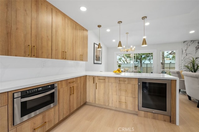 kitchen featuring wine cooler, light brown cabinetry, decorative light fixtures, kitchen peninsula, and stainless steel oven