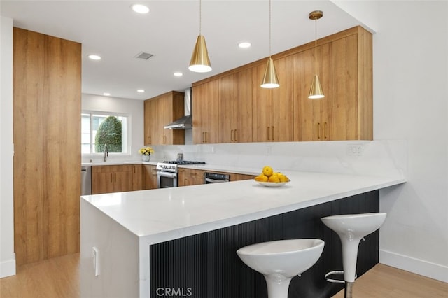 kitchen featuring sink, hanging light fixtures, gas range, kitchen peninsula, and wall chimney exhaust hood