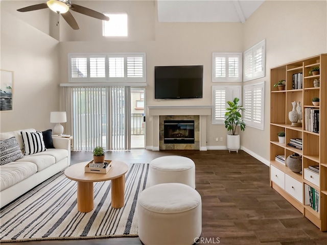 living room with a tiled fireplace, a towering ceiling, dark hardwood / wood-style floors, and ceiling fan