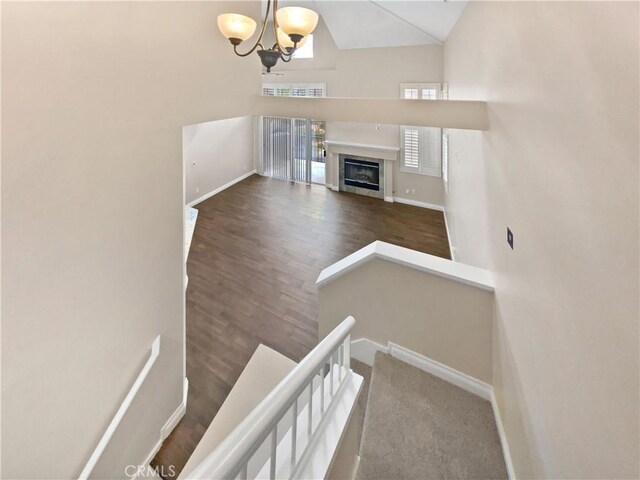 staircase featuring an inviting chandelier, high vaulted ceiling, and hardwood / wood-style flooring